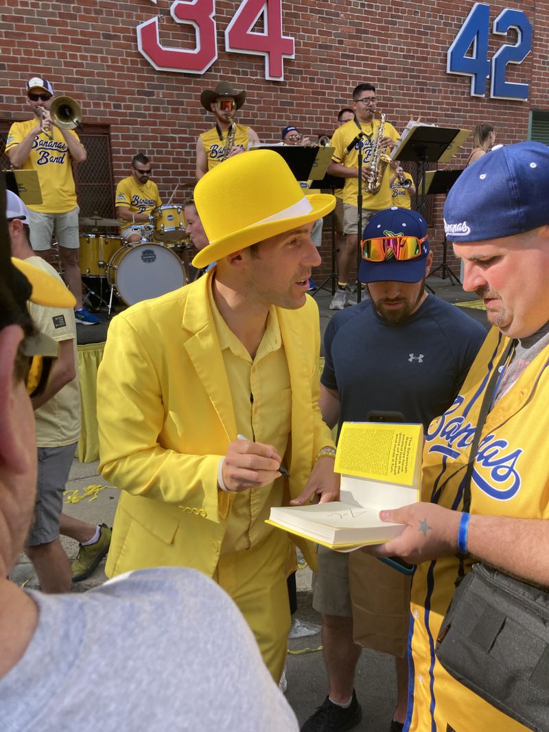 Savannah Bananas owner Jesse Coles autographs a copy of his book for a fan outside of Fenway Park on Saturday before a game against the Party Animals. (Adam Van Brimmer/AJC)
