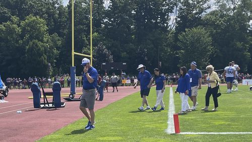 Buffalo Bills owner Terry Pegula holds his wife Kim Pegula's hand as he escorts her off the field after she met with the players in the end zone following the end of training camp in Pittsford, N.Y., Friday, July 26, 2024. (AP Photo/John Wawrow)