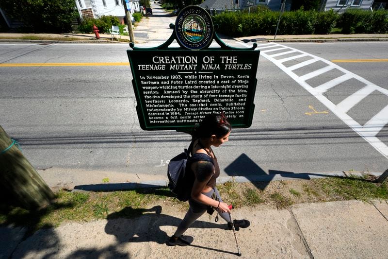 Heather Shingleton, of Dover, N.H., walks past a roadside marker honoring the local creation of the Teenage Mutant Ninja Turtles characters, Thursday, Sept. 5, 2024, in Dover. (AP Photo/Charles Krupa)