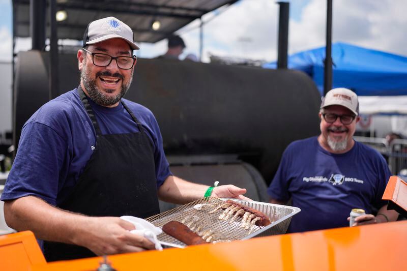 Adriano Pedro, left, and Bruno Panhoca of Brazil smile as they pull lamb from the grill at the World Championship Barbecue Cooking Contest, Friday, May 17, 2024, in Memphis, Tenn. The two are members of the Pig Diamonds team that includes members from the United States and Brazil. (AP Photo/George Walker IV)