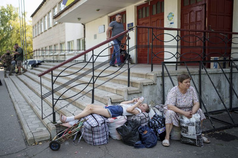 Tetiana, 11, lays on their possessions as she and her grandmother Tetiana, 61, wait for transfer to the train station during the evacuation of local people from Selidove to safe areas, in Pokrovsk, Donetsk region, Ukraine, on Tuesday, Aug. 20, 2024. (AP Photo/Evgeniy Maloletka)