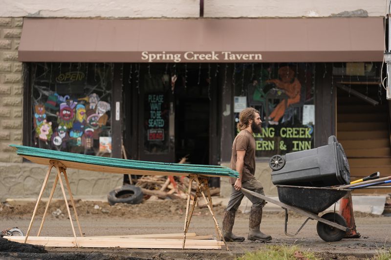 A person pushes a wheelbarrow and trash can as clean up in the aftermath of Hurricane Helene begins Tuesday, Oct. 1, 2024, in Hot Springs, N.C. (AP Photo/Jeff Roberson)