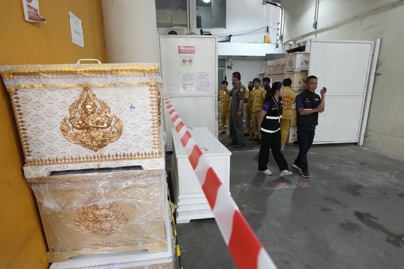 Forensic officers stand beside empty coffins at a forensic police hospital in Bangkok, Thailand, Wednesday, Oct. 2, 2024, following a deadly bus fire incident. (AP Photo/Sakchai Lalit)