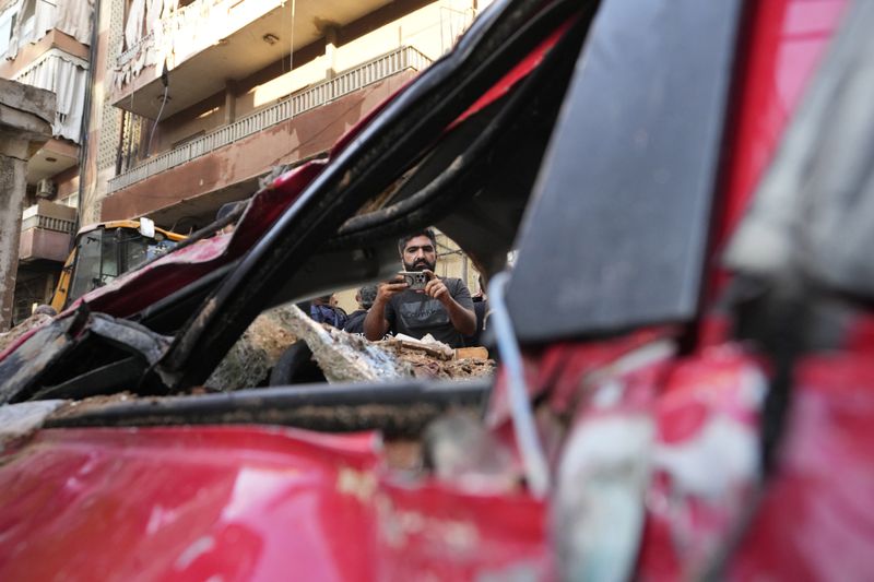 A man uses his mobile phone to document a damaged car at the scene of the building that was hit by an Israeli airstrike in Beirut's southern suburbs, Tuesday, Sept. 24, 2024. (AP Photo/Hassan Ammar)