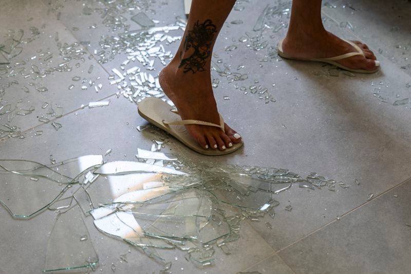 A woman stands on broken glass from the window in her bedroom following an attack from Lebanon, in Acre, north Israel, Sunday, Aug. 25, 2024. (AP Photo/Ariel Schalit)