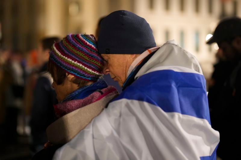 A man embraces a women at they attend the reading the names of the victims of the Hamas attack on Israel, during a commemoration to mark the first anniversary of the attack, at the Brandenburg Gate in Berlin, Germany, Monday, Oct. 7, 2024. (AP Photo/Markus Schreiber)