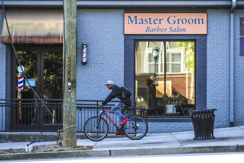 A bicycle rider pedals past the Master Groom Barber Salon in the 300 block of Decatur Street on Wednesday, April 22, 2020. Gov. Brian Kemp has defended rolling back restrictions on small businesses such as barber shops and hair salons despite federal health officials and many mayors of Georgia cities warning that it is too soon to relax measures meant to quell the coronavirus pandemic. JOHN SPINK/JSPINK@AJC.COM