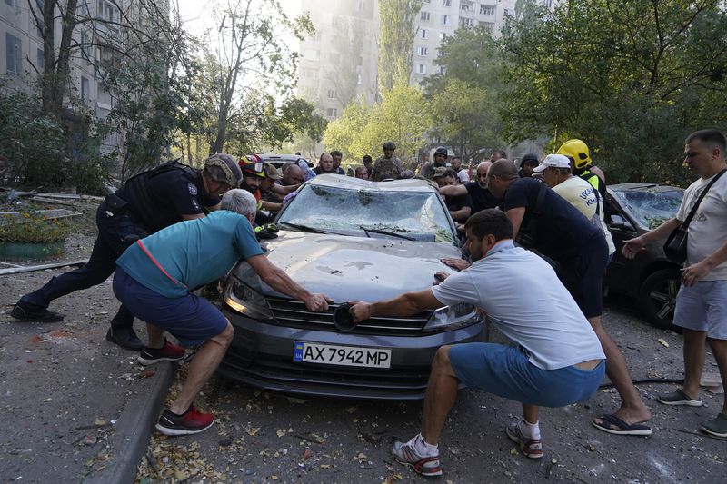 Emergency services and local residents move a damaged car after a Russian aerial bomb struck a multi-story residential building in Kharkiv, Ukraine, Sunday Sept. 15, 2024. (AP Photo/Andrii Marienko)