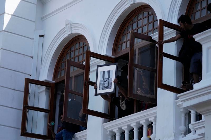 FILE - A protester holds a portrait of former Sri Lankan Prime Minister Mahinda Rajapaksa upside down after storming the Prime Minister Ranil Wickremesinghe's office demanding he resign after president Gotabaya Rajapaksa fled the country amid economic crisis, in Colombo, Sri Lanka, on July 13, 2022. (AP Photo/Eranga Jayawardena, File)