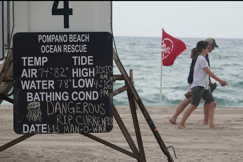FILE - Beachgoers walk past warning flags and signs, Jan. 13, 2020, in Pompano Beach, Fla. About 100 people drown from rip currents along U.S. beaches each year, according to the U.S. Lifesaving Association, and more than 80 percent of beach rescues annually involve rip currents. (Joe Cavaretta/South Florida Sun-Sentinel via AP, File)