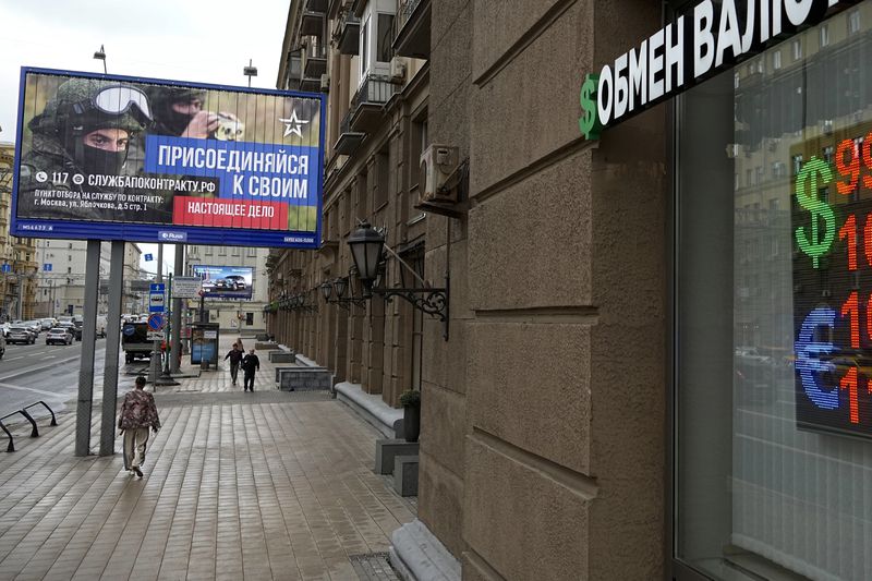 FILE - People walk past a currency exchange office with an army recruiting billboard calling for a contract for service in the Russian armed forces in Moscow, Russia,on Aug. 14, 2023. (AP Photo, File)