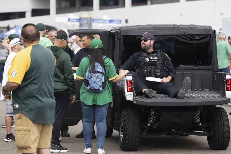 A police officer interacts with fans outside the Oakland Coliseum before a baseball game between the Oakland Athletics and the Texas Rangers Thursday, Sept. 26, 2024, in Oakland, Calif. (AP Photo/Benjamin Fanjoy)