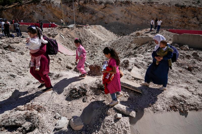 People carry their luggage as they cross into Syria on foot, through a crater caused by Israeli airstrikes aiming to block Beirut-Damascus highway at the Masnaa crossing, in the eastern Bekaa Valley, Lebanon, Saturday, Oct. 5, 2024. (AP Photo/Hassan Ammar)