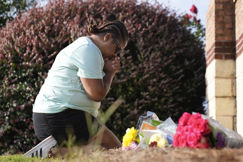 Linda Carter, of Grayson, Ga., kneels near Apalachee High School to place flowers as she mourners for the slain students and teachers on Thursday, Sept. 5, 2024, in Winder, Ga. (AP Photo/Brynn Anderson)