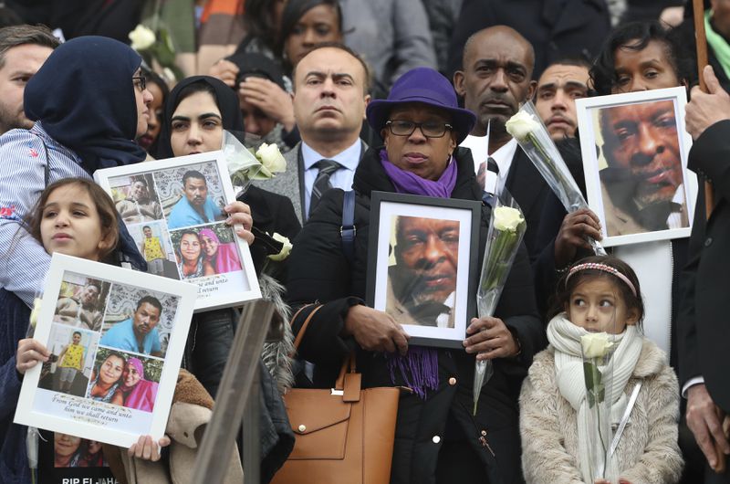 FILE - People hold up photos of their loved ones, victims of the fire, as they leave the Grenfell Tower National Memorial Service at St Paul's Cathedral, in London, Thursday Dec. 14, 2017. (Gareth Fuller/Pool Photo via AP, FIle)