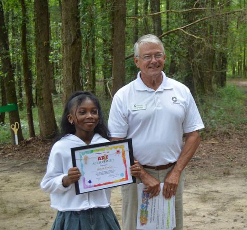 Mayor Vince Evans presents a certificate to 10-year-old Tionne Brown, who designed one of the blue heron statues. Her design theme was 'Kaleidoscope of Colors.' (Photo Courtesy of Alice Queen)