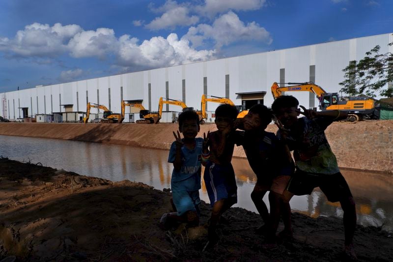 Children pose in front of bulldozers lined along the Funan Techo canal at Prek Takeo village, eastern Phnom Penh, Cambodia, Tuesday, July 30, 2024. (AP Photo/Aniruddha Ghosal)