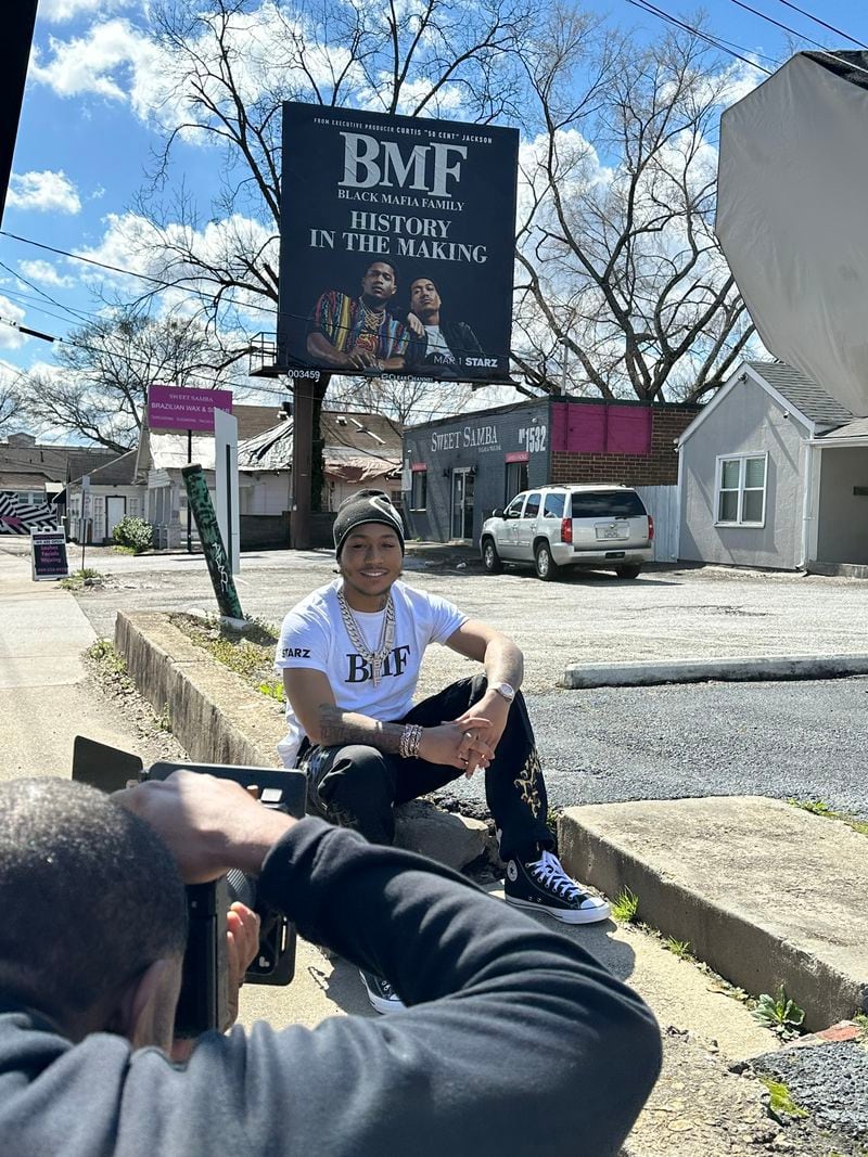 Demetrius Flenory Jr., who plays his father in Starz' "BMF," posted for Starz  photos in front of a Starz promotional billboard on Howell Mill Road Road Feb. 24, 2024 in homage to real BMF billboards back in the 2000s. RODNEY HO/rho@ajc.com