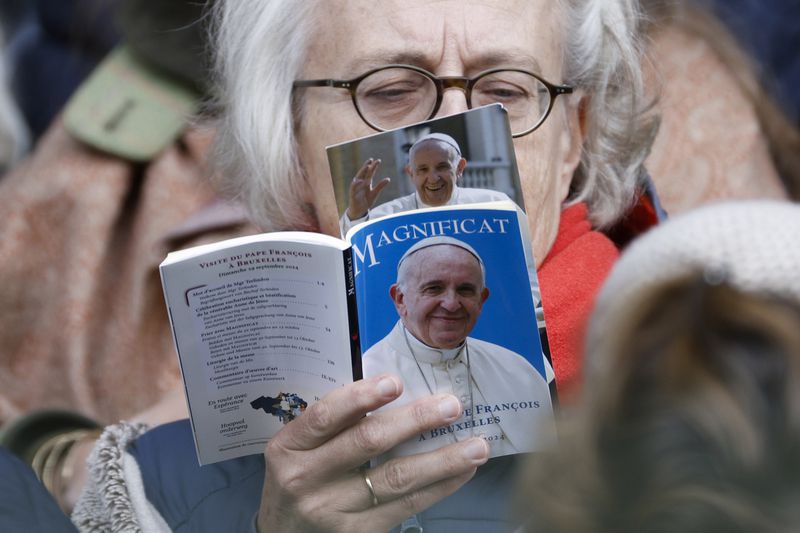 A faithful reads a book as Pope Francis presides the holy mass, at the King Baudouin stadium in Brussels, Belgium, Sunday, Sept. 29, 2024. (AP Photo/Omar Havana)