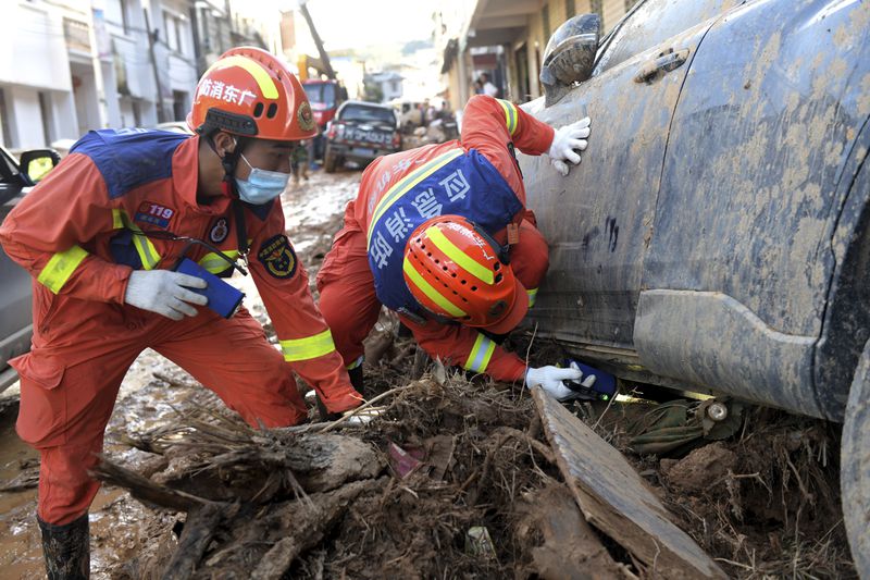 In this photo released by Xinhua News Agency, rescuers look under a vehicle in a flood-affected area in Sishui Township of Pingyuan County, Meizhou City, southern China's Guangdong Province, Thursday, June 20, 2024. Multiple people have died and several people were reported missing after downpours in recent days caused historic flooding in rural parts of Guangdong province in southern China, while authorities warned Friday of more flooding ahead in other parts of the country. (Lu Hanxin/Xinhua via AP)
