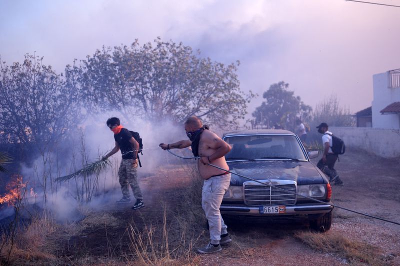 Volunteers try to extinguish the flames near a house during a fire in northern Athens, Monday, Aug. 12, 2024, as hundreds of firefighters tackle a major wildfire raging out of control on fringes of Greek capital. (AP Photo/Aggelos Barai)