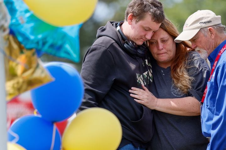  April Johnson, pictured at the center, embraced her 11th-grade son, Gavin, a student at Apalachee High School, as they paid their respects by the flagpole. This moment occurred a day after a tragic event at a Barrow County high school in which a 14-year-old opened fire on Wednesday morning, resulting in the loss of two students and two teachers and injuring nine others. Thursday, September 5, 2024, (Miguel Martinez/AJC)