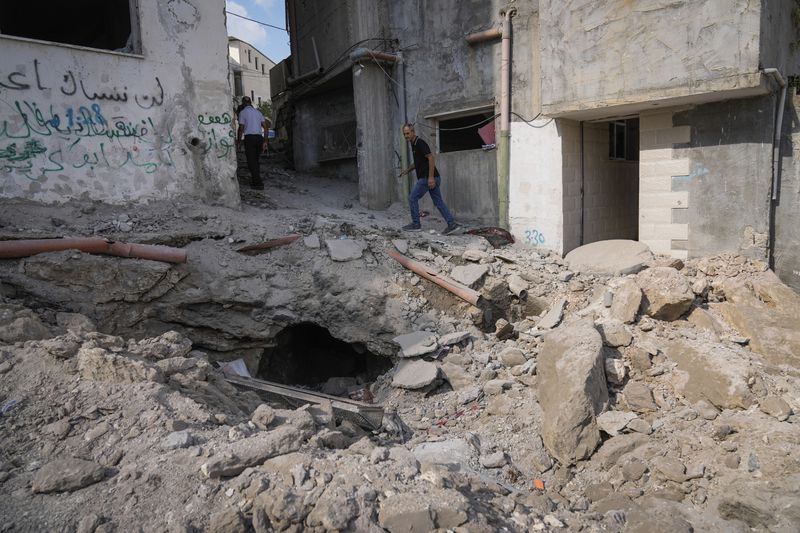 Palestinians walk past a damaged building following an Israeli military operation in the West Bank city of Jenin on Friday, Sept. 6, 2024. (AP Photo/Majdi Mohammed)