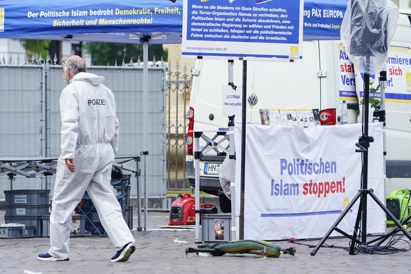 A forensic police officers walks past a smashed stall which had a banner with writing reading "Stop political Islam", on the market square in Mannheim, Germany, Friday, May 31, 2024. An assailant with a knife attacked and wounded several people in a central square in the southwestern German city of Mannheim on Friday, police said. Police shot the attacker, who also was hurt. (Uwe Anspach/dpa via AP)