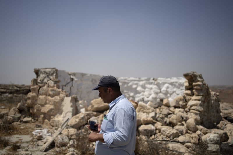 Fayez Suliman Tel, head of the village council for Khirbet Zanuta, stands next to a home that was destroyed when his community was driven out by Israeli settlers, Tuesday, Aug. 27, 2024. Ten months after settlers threatened to kill them if they didn't leave their West Bank village, some Palestinian residents are finally home, under a rare court order. (AP Photo/Maya Alleruzzo)