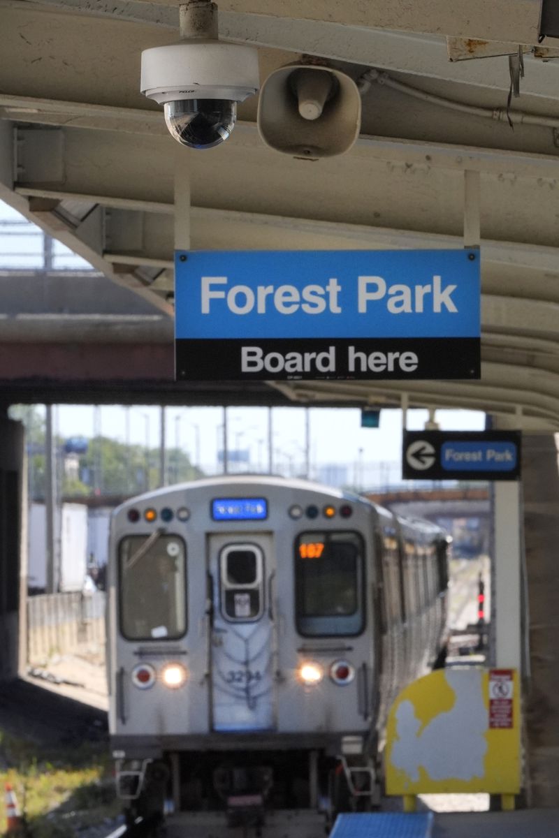 A security camera and speaker hang from the ceiling of the Chicago Transit Authority Harlem Ave. station as a Blue Line train enters the station heading West to the Forest Park, Ill., station as two pedestrians walk toward the station, Tuesday, Sept. 3, 2024, in Forest Park, Ill. (AP Photo/Charles Rex Arbogast)