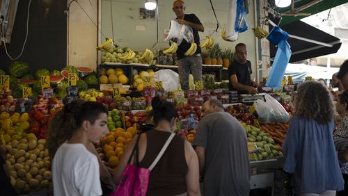 People buy fruit from a street market in Haifa, Israel, Friday, Aug. 16, 2024. Israel's economy is suffering from the nearly 11-month war with Hamas, as its leaders grind ahead with its offensive in Gaza that threatens to escalate into a wider conflict. (AP Photo/Leo Correa)