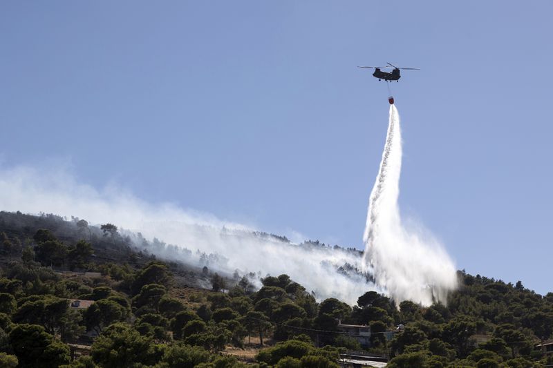 A firefighting helicopter throws water over a wildfire at Keratea area, southeast of Athens, Greece, Sunday, June 30, 2024. (AP Photo/Yorgos Karahalis)