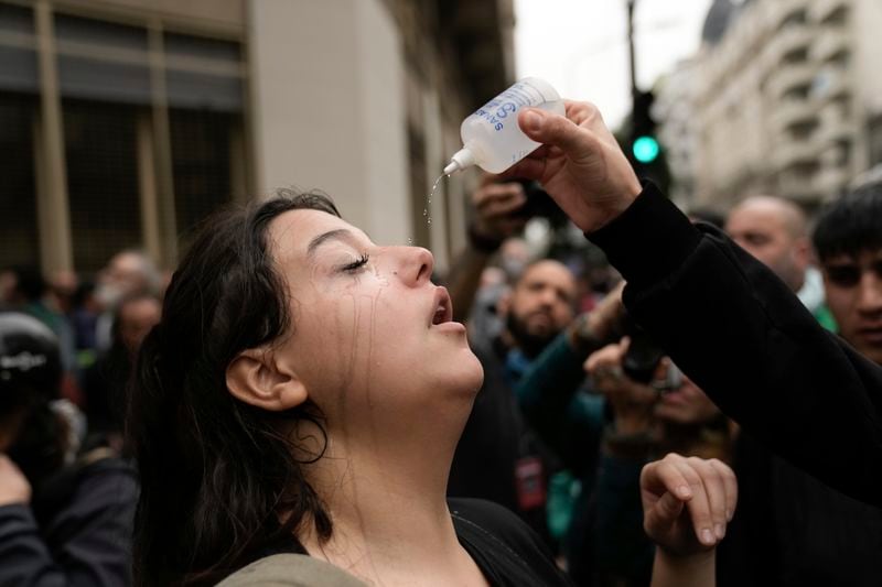 An anti-government protester tries to alleviate the effect of gas sprayed by police outside Congress where lawmakers debate a reform bill promoted by Argentine Javier Milei in Buenos Aires, Argentina, Wednesday, June 12, 2024. (AP Photo/Rodrigo Abd)