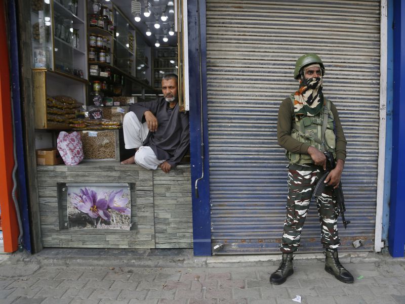 An Indian paramilitary soldier stands guard as a Kashmiri shopkeeper waits for customers in Srinagar, Indian controlled Kashmir, Monday, July 1, 2019. (AP Photo/Mukhtar Khan, File)