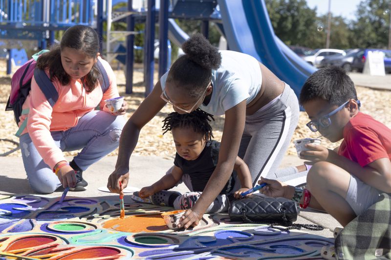 Children paint a display on the ground at a back to school health fair in Milwaukee, on Saturday Aug. 10, 2024. (AP Photo/Jeffrey Phelps)