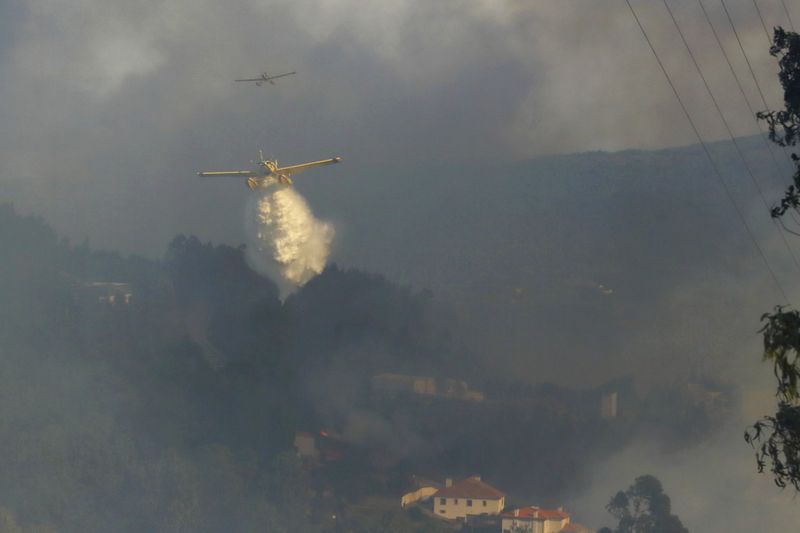 Firefighting airplanes drop water on a fire burning near houses in Sever do Vouga, a town in northern Portugal that has been surrounded by forest fires, Monday, Sept. 16, 2024. (AP Photo/Bruno Fonseca)