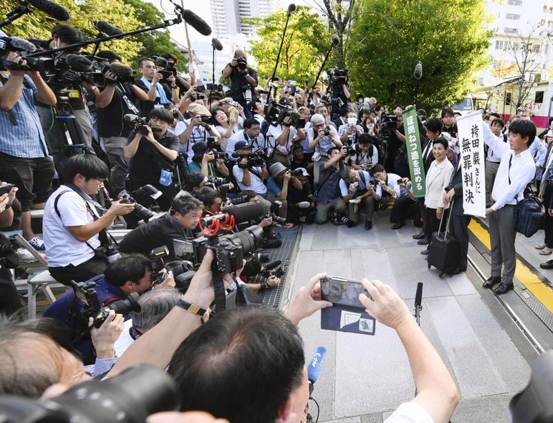 Hideko Hakamada, center at right side, sister of 88-year-old former boxer Iwao Hakamada who has been on death row for nearly six decades after his murder conviction that his lawyers said was based on forced confession and fabricated evidence, is surrounded by journalists after a court ruled that her brother was not guilty in a retrial for a 1966 quadruple murder, in front of the court in Hamamatsu, Shizuoka prefecture, Thursday, Sept. 26, 2024. The signs read "Acquittal to Mr. Iwao Hakamada, " right, and "Acknowledged fabrications of evidence." (Kyodo News via AP)