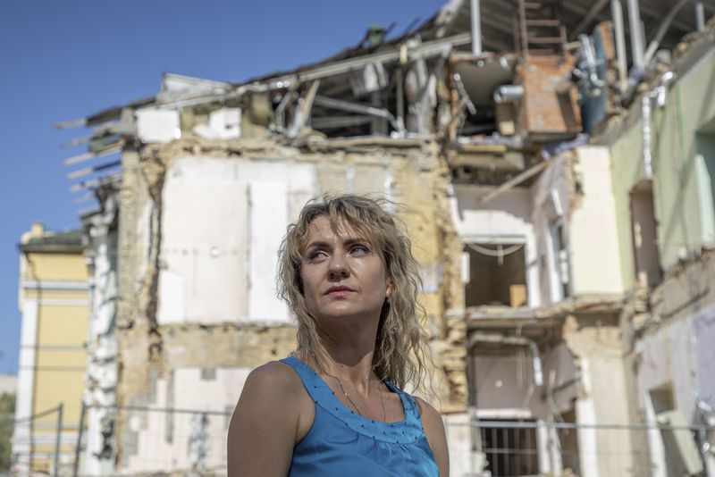 Maryna Berdar, 39, co-founder of the "Bureau of Smiles and Support" sits in front of Okhmatdyt children's hospital in Kyiv, Ukraine Saturday Sept. 14, 2024 which was destroyed after a Russian missile strike on July 8. (AP Photo/Anton Shtuka)