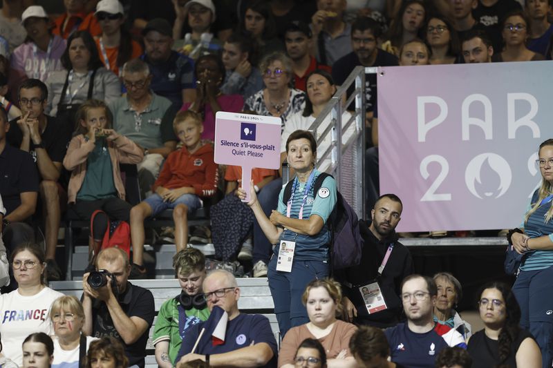 A volunteer for the Paralympic Games holds a sign reading "Silence s'il-vous-plaît, Quiet Please" during the mens' United States versus France goalball game during the Paralympic Games in Paris on Saturday, Aug. 31, 2024. Football fans are known for being loud and rowdy. But the Paralympic sports most closely related to football, blind football and goalball, require spectators to be silent during game action so that players can receive audible cues from the ball and the environment. (AP Photo/Felix Scheyer)