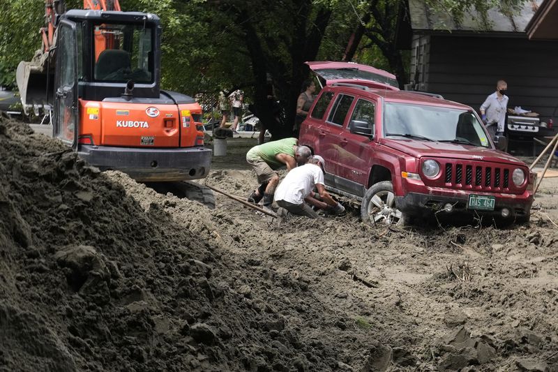 Two men dig out an SUV stuck in the mud along Hudson Avenue after remnants of Hurricane Beryl caused flooding and destruction, Friday, July 12, 2024, in Plainfield, Vt. (AP Photo/Charles Krupa)