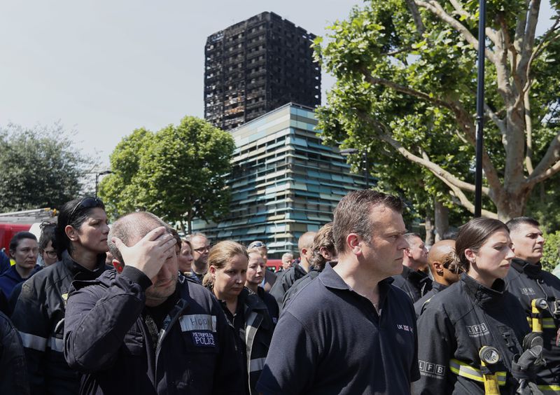 FILE - Emergency services workers take part in a minute's silence in front of Grenfell Tower in London, Monday, June 19, 2017. (AP Photo/Kirsty Wigglesworth, File)