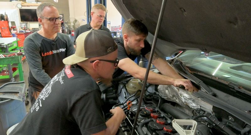Ryan Burton (left) and Bill Conley watch as mechanics work on a car at Conley's Neighborhood Automotive Service in Cumming. Burton's marketing company has grown, but it's sometimes hard to find new employees. Under the hood are Gary Simmons and Joshua Evans 
