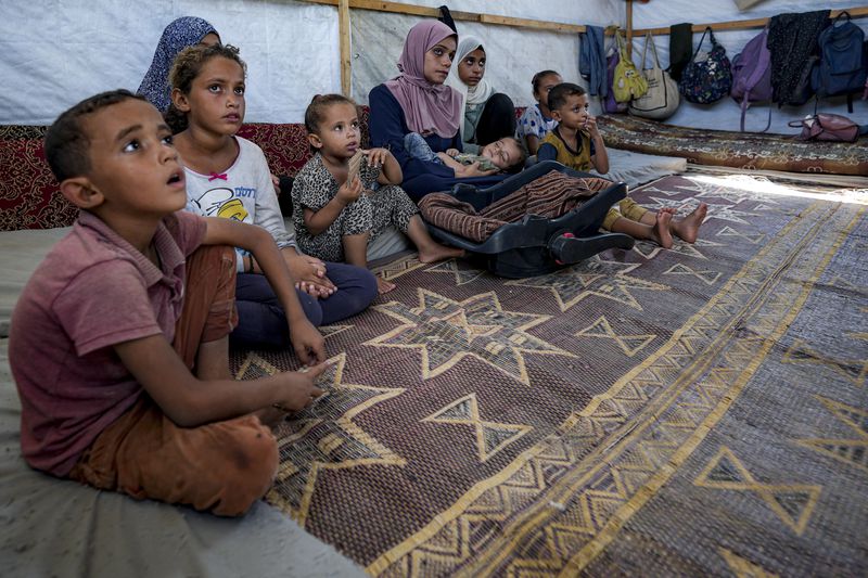 Displaced infant Abdel-Rahman Abuel-Jedian, 11-month-old, who suffers from polio, is carried by his mother, center, at a makeshift tent camp in Deir al-Balah, central Gaza Strip, Tuesday, Aug. 27, 2024. (AP Photo/Abdel Kareem Hana)