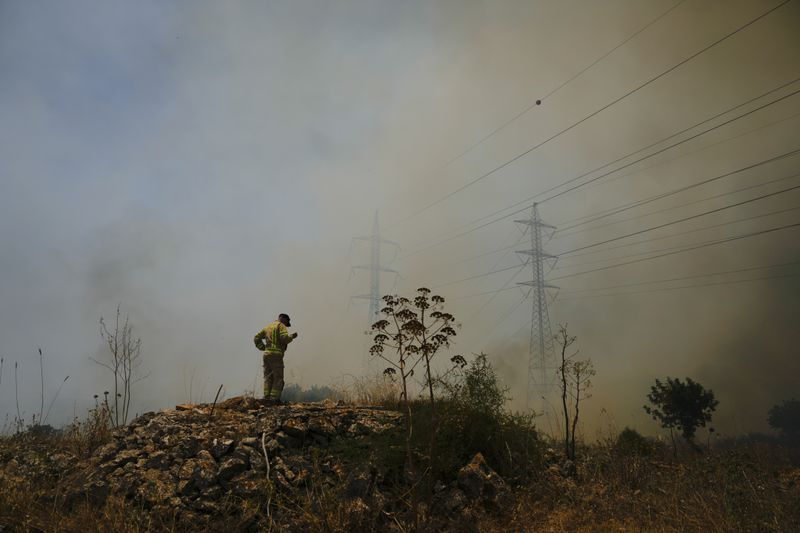 An Israeli firefighter stands next to fire burning in an area near the community of Ramot Naftali, by the border with Lebanon, northern Israel, Tuesday, June 4, 2024. The Israeli military said Tuesday that six soldiers were lightly injured in a brush fire in the country's north that was sparked by fighting with the Lebanese militant group Hezbollah. (AP Photo/Ariel Schalit)