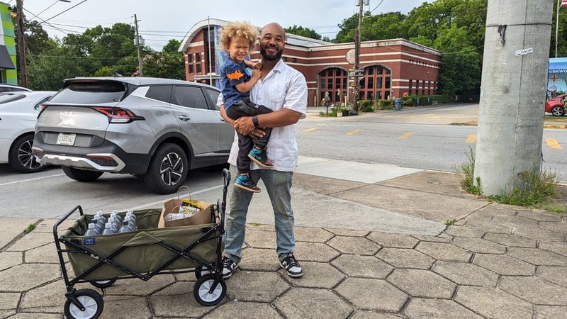 Jonathan Colbert, 39, holds his son Axel, 3, next to a wagon filled with water bottles in Kirkwood on Saturday.