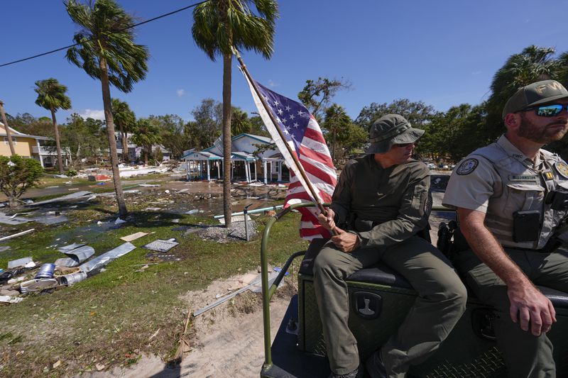 Officer Nate Martir, a law enforcement officer from the Florida Fish Wildlife and Conservation Commission, holds an American flag that was lying on the ground amid debris, while patrolling from a high water capable swamp buggy, in the aftermath of Hurricane Helene, in Cedar Key, Fla., Friday, Sept. 27, 2024. (AP Photo/Gerald Herbert)