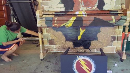 Artist Leilani Saxon prepares “Barry,” a piano whose paint scheme was inspired by the superhero “The Flash,” for its public debut Sunday, Aug. 5, at Webb Bridge Park in Alpharetta. PLAY ME AGAIN PIANOS