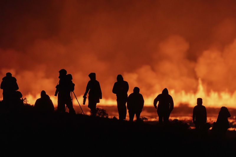 Tourists and visitors try to get a view of the eruption from a distance from the intersection between Reykjanesbraut, Iceland, and the road to Grindavik, Thursday, Aug. 22, 2024. (AP Photo/Marco di Marco)