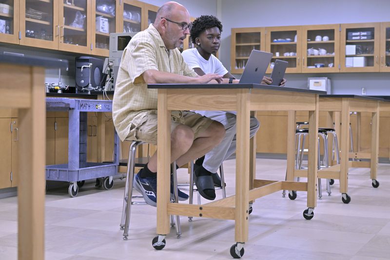 History teacher Matt Brophy, left, works with Flerentin “Flex” Jean-Baptiste, 16, of Medford, Mass., on making up late assignments during summer school at Medford High School, Friday, Aug. 2, 2024, in Medford. (AP Photo/Josh Reynolds)