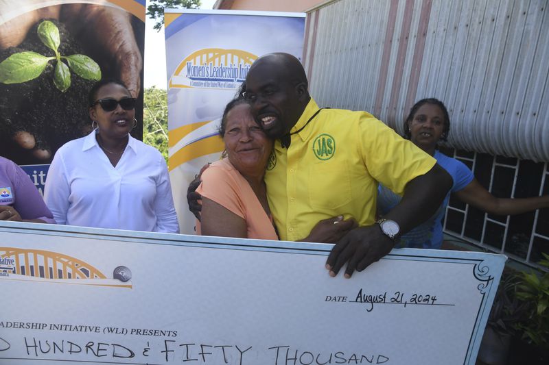 Alance Wisdom is hugged by Norman Murray during a check presentation on Thursday, Aug. 22, 2024, in Cross Keys, Jamaica. (AP Photo/Collin Reid)